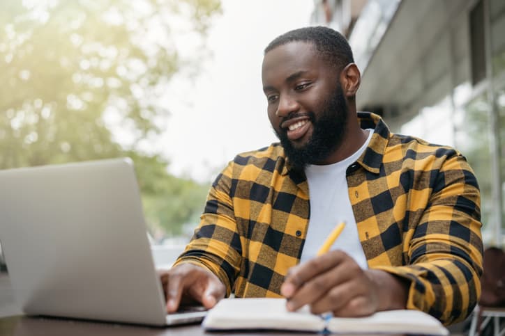 年轻英俊的非裔美国房地产估价师使用笔记本电脑，记笔记，在线学习